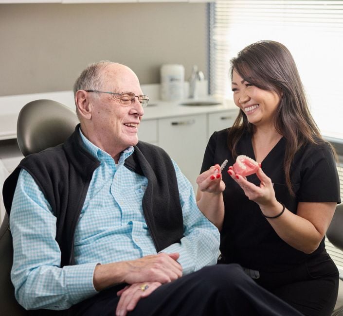 dentist smiling and showing elderly man patient how to use Invisalign
